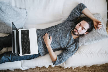 Mann mit Laptop schlafend auf Sofa zu Hause - EBBF01812