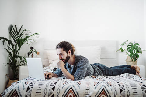 Young man working on laptop while lying on bed at home stock photo