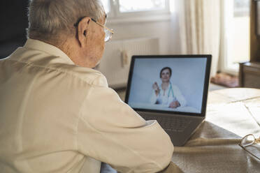 Älterer Mann lässt sich von einer Ärztin auf Video über einen Laptop im Wohnzimmer beraten - UUF22261