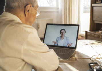 Eine Ärztin berät einen älteren männlichen Patienten während eines Videoanrufs zu Hause - UUF22266