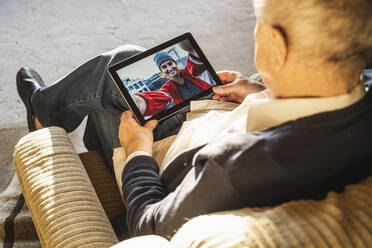Grandfather talking with granddaughter on video call through digital tablet at home - UUF22268