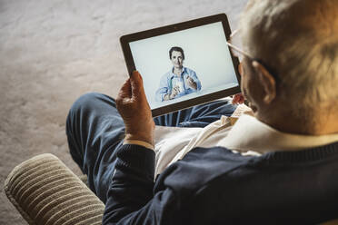 Senior man taking advice from female general practitioner on video call through digital tablet - UUF22269