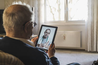 Senior man taking advice from male doctor on video call through digital tablet at home - UUF22272