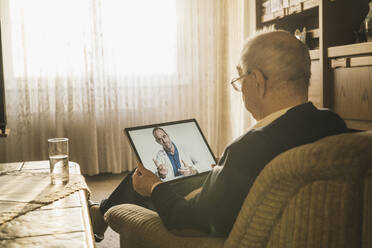 Älterer Mann lässt sich von einem männlichen Arzt per Videoanruf beraten, während er zu Hause auf dem Sofa sitzt - UUF22277