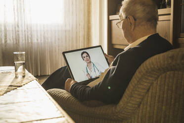 Female doctor advising male patient on video call over digital tablet in living room - UUF22280