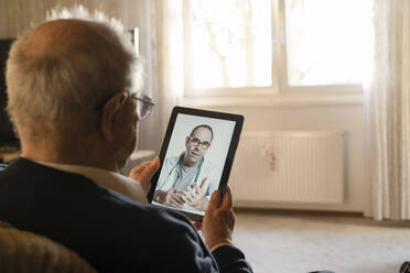 General practitioner consulting senior man online through digital tablet in living room - UUF22283