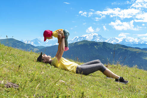 Mutter hebt ihr kleines Mädchen im Gras liegend am Col des Aravis auf, Haute-Savoie, Frankreich - GEMF04479