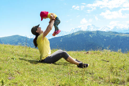 Verspielte Mutter mit ihrem Kind beim Spielen im Gras am Col des Aravis, Haute-Savoie, Frankreich - GEMF04480