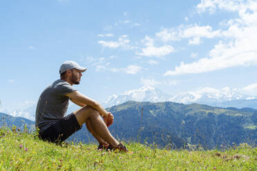 Erwachsener Mann, der über Gras am Col des Aravis, Haute-Savoie, Frankreich, sitzt und nachdenkt - GEMF04481