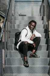 Man with cool attitude sitting on steps during sunny day - EBBF01849