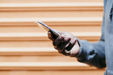 Young man with smart phone by brown corrugated wall - EBBF01857