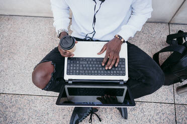 Mann trinkt Kaffee auf dem Bürgersteig, während er am Laptop arbeitet - EBBF01869
