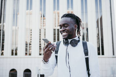 Smiling man with mobile phone against building in city - EBBF01878