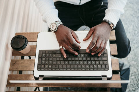 Junger Mann mit Laptop in einem Café sitzend, lizenzfreies Stockfoto