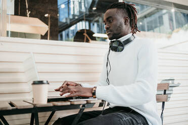 Creative businessman with disposable coffee cup working on laptop in cafe - EBBF01886