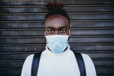 Junger Mann mit Gesichtsschutzmaske an einer Wellblechwand - EBBF01894
