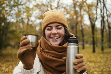 Glückliche Frau mit Strickmütze und Edelstahlflasche im Herbstpark - OYF00278