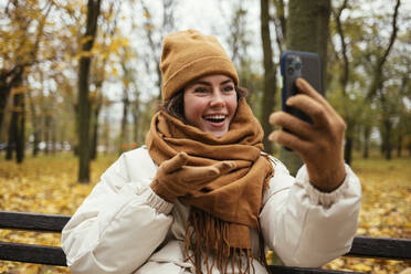 Happy young woman in knit hat on video call at autumn park - OYF00288