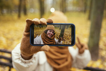 Junge Frau zeigt Selfie auf Handy im Herbst Park - OYF00290