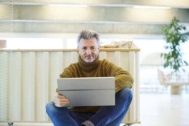Lächelnder reifer Mann, der ein digitales Tablet benutzt, während er zu Hause sitzt - FMKF06845