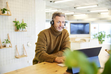 Businessman with headset talking while using digital tablet at office - FMKF06853