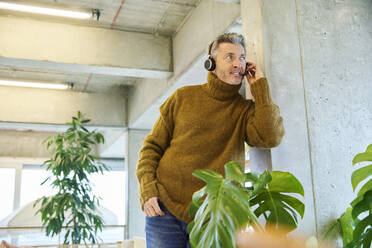 Geschäftsmann mit Headset im Gespräch, während er sich auf eine Säule im Büro stützt - FMKF06858