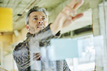 Businessman planning while standing by glass wall at office - FMKF06882