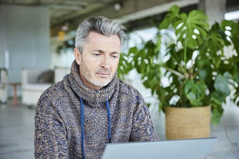 Mann, der ein digitales Tablet benutzt, während er im Büro sitzt - FMKF06896