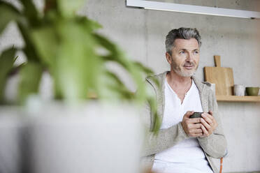 Thoughtful man holding coffee cup while sitting at home - FMKF06917