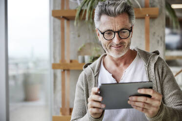 Mature man smiling while using digital tablet - FMKF06931