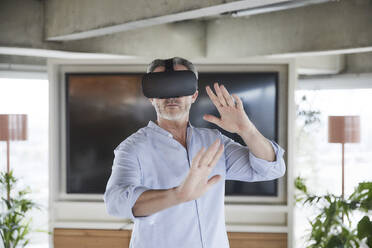 Businessman wearing virtual reality headset standing at home - FMKF06945