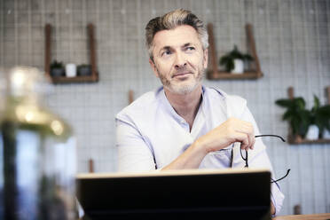 Thoughtful businessman with digital tablet looking away - FMKF06950