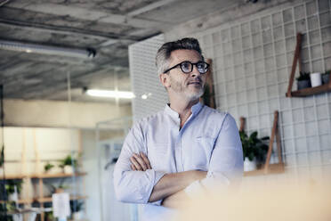 Businessman wearing eyeglasses looking away while standing with arms crossed - FMKF06951