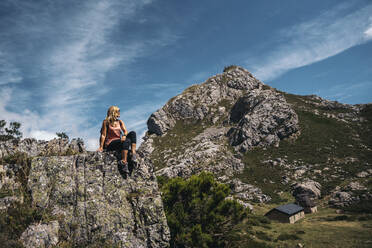 Frau schaut weg, während sie an einem sonnigen Tag auf einem Felsenberg sitzt - MPPF01323