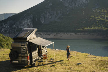 Woman looking at lake while standing by camper van during vacation - MPPF01324