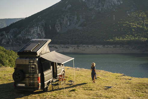 Woman looking at lake while standing by camper van during vacation - MPPF01324