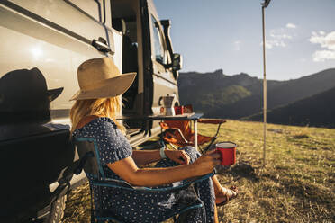 Mittlere erwachsene Frau mit Hut trinkt an einem sonnigen Tag Kaffee am Wohnmobil - MPPF01328
