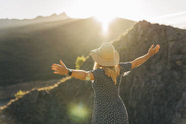 Woman with arms raised standing in front of mountain on sunny day - MPPF01334