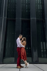 Heterosexuelles Paar, das sich in einer Umarmung vor einem Gebäude anschaut - OGF00673