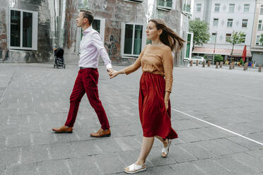 Heterosexuelles Paar hält sich an den Händen, während es auf der Straße in der Stadt spazieren geht - OGF00687