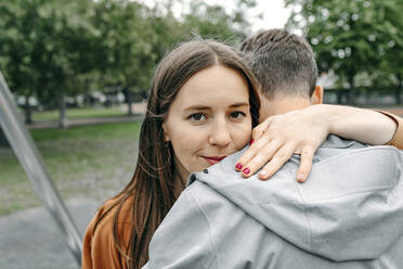 Smiling girlfriend embracing boyfriend in public park - OGF00696