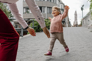 Fröhliche Tochter läuft auf ihren Vater zu, während sie auf der Straße in der Stadt spielt - OGF00699