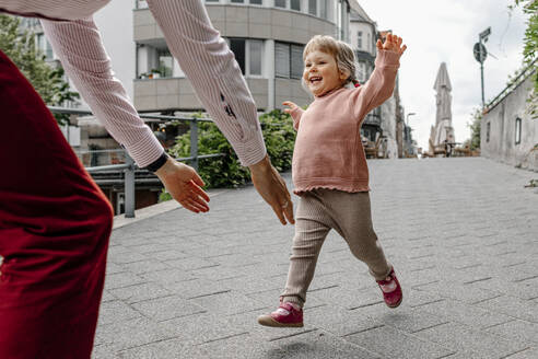 Cheerful daughter running towards her father while playing on street in city - OGF00699