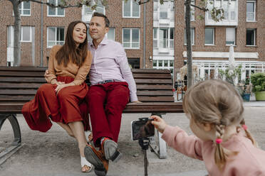 Daughter taking photograph of parents through mobile phone while sitting on park bench - OGF00700