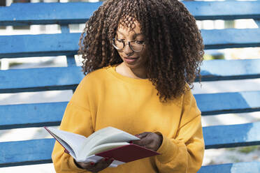 Lächelnde junge Frau, die auf der Tribüne sitzend ein Buch liest - PNAF00283