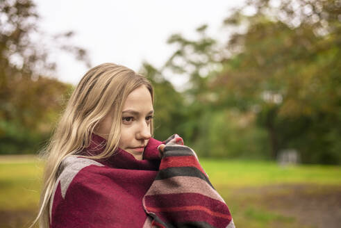 Young woman wrapped in scarf at park during autumn - BFRF02331