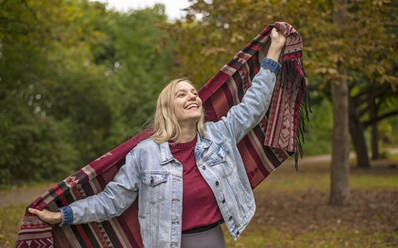 Glückliche Frau mit Schal im herbstlichen Park stehend - BFRF02332