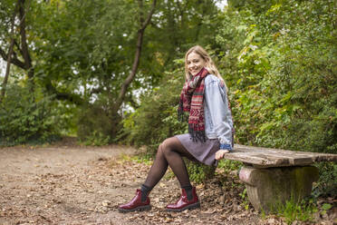 Attractive woman sitting on bench in autumnal park - BFRF02334