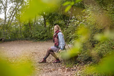 Thoughtful smiling woman looking away while sitting on bench in park - BFRF02335