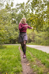 Cheerful woman running in park during autumn - BFRF02338